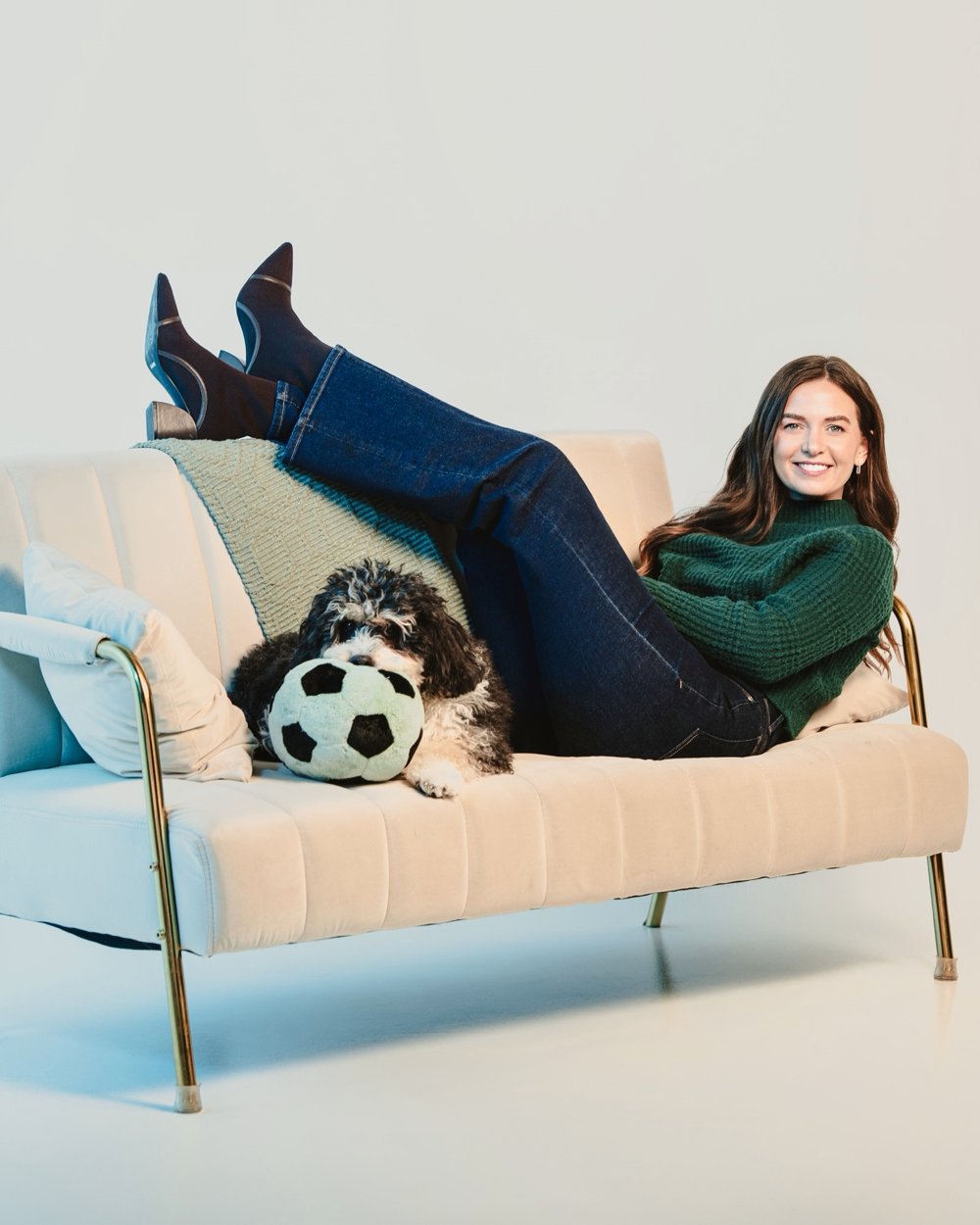 Nicole lounging on a cream sofa with her dog and a plush soccer ball