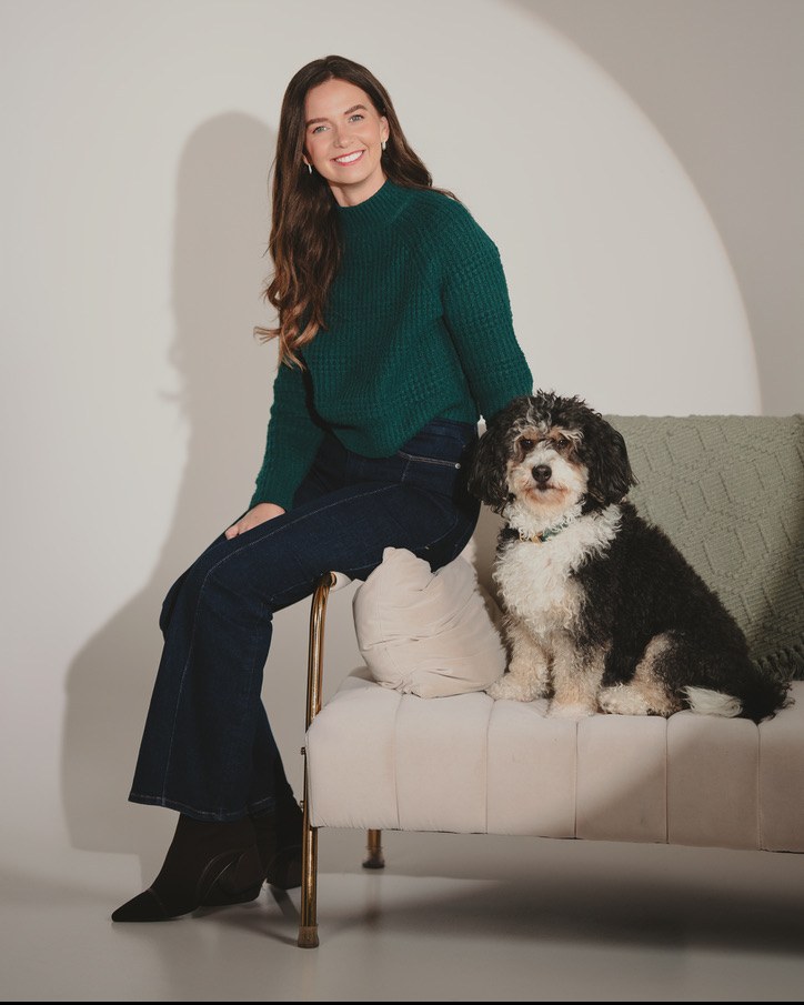 Nicole in a green sweater sitting on a cream bench beside her dog