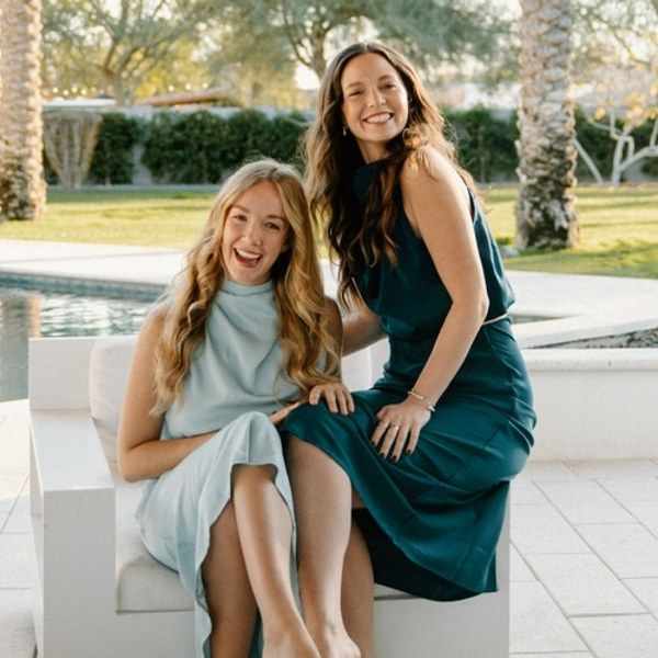 Nicole laughing with a friend by the pool, both in soft teal dresses